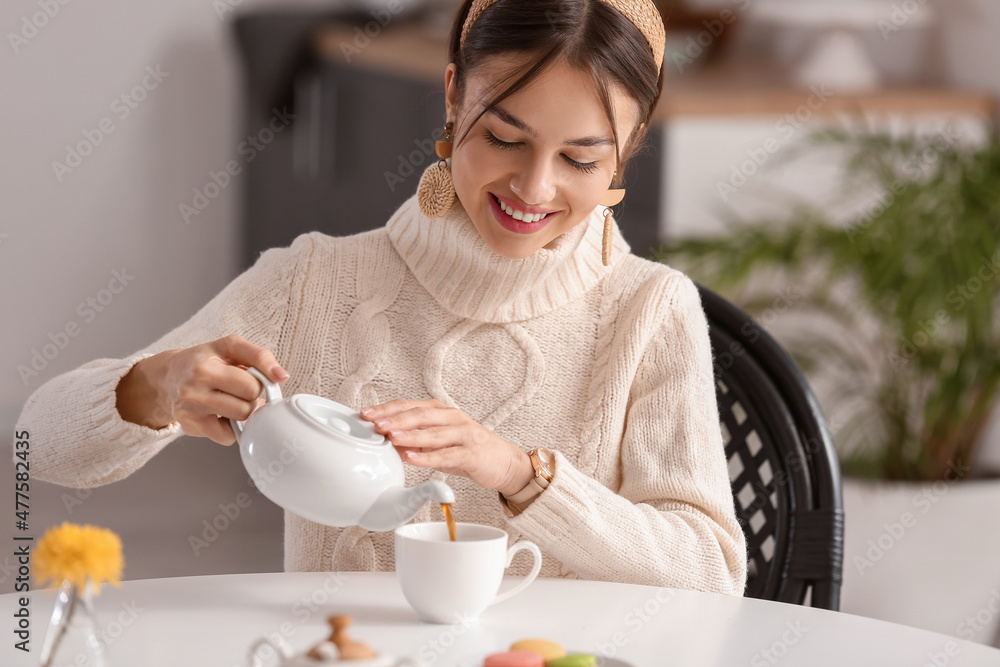 Beautiful young woman drinking tasty tea at table in cafe