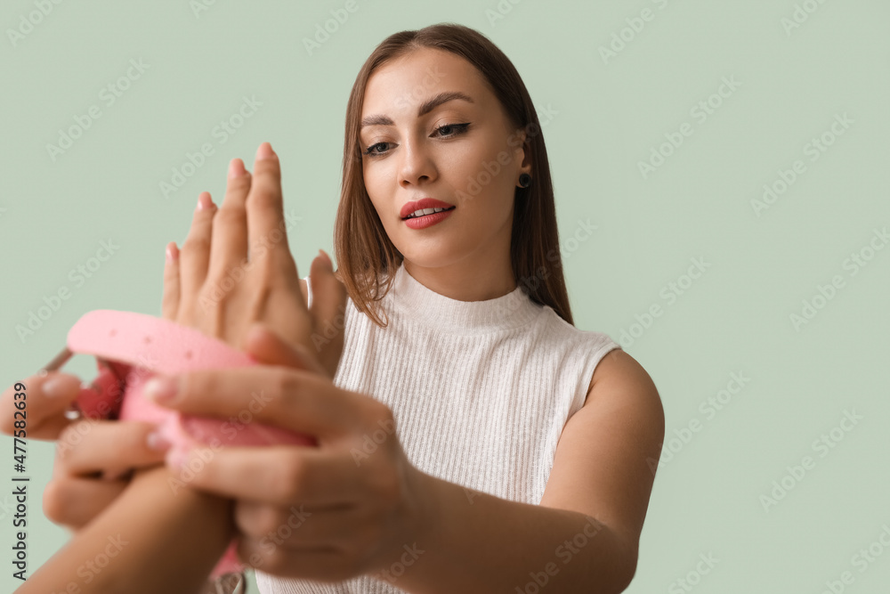 Young woman putting handcuffs from sex shop on her partner against color background