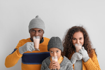 Poster - African-American family in winter clothes drinking tasty hot chocolate on light background