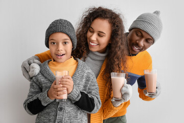 Canvas Print - African-American family in winter clothes and with tasty hot chocolate on light background