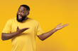 © ViDi Studio - Young smiling happy black man 20s wearing bright casual t-shirt point hands arms aside on workspace area mock up isolated on plain yellow color background studio portrait. People lifestyle concept