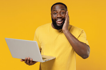 Wall Mural - Young smiling copywriter fun happy black man 20s wearing bright casual t-shirt hold use work on laptop pc computer isolated on plain yellow color background studio portrait People lifestyle concept