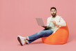 © ViDi Studio - Full body young fun happy man in trendy jacket shirt sit in bag chair hold use work point finger on laptop pc computer isolated on plain pastel light pink background studio. People lifestyle concept.