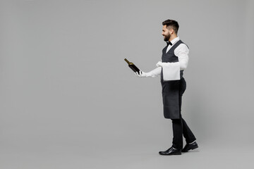 Wall Mural - Full size young barista male waiter butler man 20s wear white shirt vest elegant uniform work at cafe give bottle of wine isolated on plain grey background studio portrait Restaurant employee concept