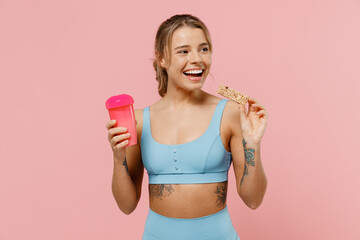 Young strong sporty fitness trainer instructor woman in blue tracksuit spend time in home gym hold cup water eat snack look aside isolated on pastel plain light pink background Workout sport concept