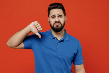 Poster - Young disappointed sad displeased unhappy man 20s wear basic blue t-shirt look camera showing thumb down dislike gesture isolated on plain orange background studio portrait. People lifestyle concept.