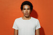 © ViDi Studio - Distempered frowning upsed unnerved severe displeased sullen aggrieved young black curly man 20s years old wear white t-shirt looking camera isolated on plain pastel orange background studio portrait
