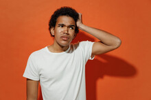 Perplexed Puzzled Bemused Concerned Young Black Curly Man 20s Years Old Wears White T-shirt Look Aside Think Put Hand On Head Have No Idea Isolated On Plain Pastel Orange Background Studio Portrait.