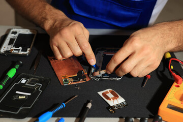 Wall Mural - Technician repairing broken smartphone at table, closeup