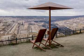 two empty deck chairs with an umbrella made of metal in front of open pit mining of hambach terra nova in germany