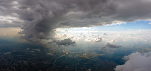 Aerial view from airplane window at high altitude of distant city covered with puffy cumulus clouds forming before rainstorm