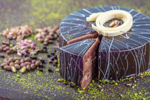 Pistachio Cake Sliced On White Wooden Background. Homemade Chocolate Cake With Dark Chocolate Glaze And Pistachios Nuts.