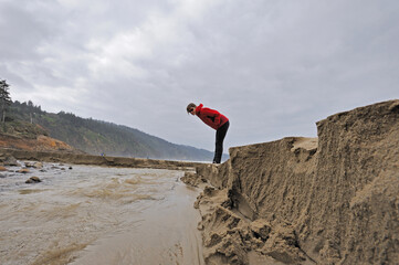 Women looks at eroding beach stream Oregon USA.