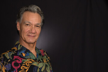 Wall Mural - Dramatic Portrait of a Mature Man against a Black Background wearing a Colorful Shirt