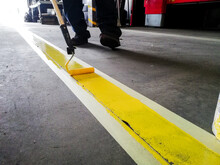 Closeup Of A Person Painting A Yellow Line On A Garage Floor Under The Lights
