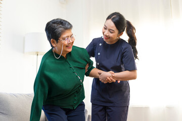 Wall Mural - Female Asian nurse help old lady stand up from a couch.