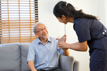 Wall Mural - Smiling nurse giving glass of water to senior asian man in nursing home or assisted living facility.