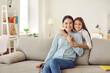 © Studio Romantic - Portrait of smiling young Caucasian mother and small teen daughter relax on couch at home on family weekend. Happy little girl child hug embrace mom show love and care, feel grateful thankful.