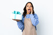 © luismolinero - Pastry chef holding a big cake over isolated white background with surprise and shocked facial expression