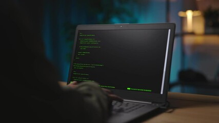 View from shoulder of woman sitting at living room during evening time and typing data code on modern laptop. Concept of programming and technology.