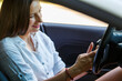 © skumer - Young woman sitting inside the car and using cellphone.