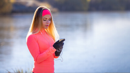 Wall Mural - Young sporty woman checking her fitness tracker on smartphone during morning running.