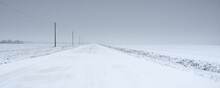 Snow-covered Rural Road Through The Field After A Blizzard. Electricity Line, Transformer Poles. Panoramic View From The Car. Dark Stormy Sky. Off-road, Logistics, Winter Tires, Remote Village