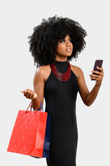 Wall Mural - portrait of a young dark-skinned woman she holds shopping bags and a cell phone, looks in an upward direction checking the information seen on her cell phone, isolated on gray background.