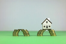 Scale Model House Sitting Across Stacks Of Pound Coins. Financial Bridging Loan Concept.