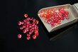 Red Songea small round sapphire gemstones lot on scoop tweezer. Fancy red, pink, orange colored gems. Beryllium diffusion treatment applied. Loose transparent clean stone settings. Black background.