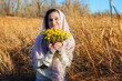 © Arsentyev Vladimir - A happy, satisfied girl in a field in the fall holds yellow wildflowers, looks into the camera. Dressed in casual clothes, sweater, scarf