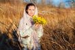 © Arsentyev Vladimir - A serious girl in a field in the fall holds yellow wildflowers, looks into the camera. Dressed in casual clothes, sweater, with a scarf on her head