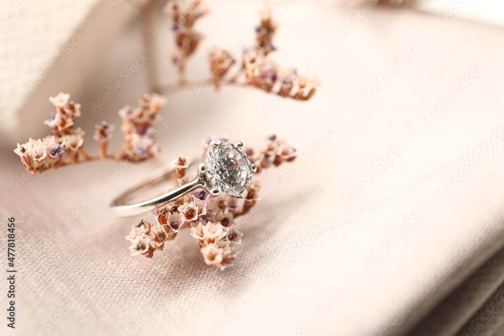 Silver engagement ring with flowers on light fabric background, closeup