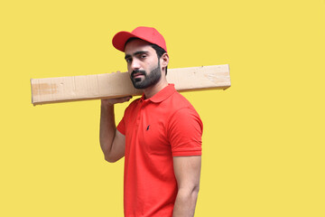 delivery man in red t shirt and cap holding packing box yellow background  indian pakistani model