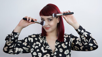 Woman holding two make-up brushes. Beautiful smiling redhead girl holding makeup brushes in front of her face. White background.