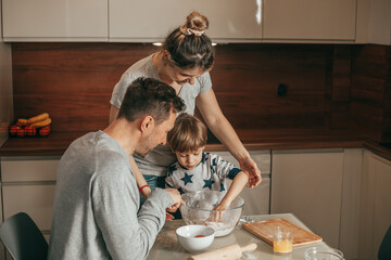 Dad and Mom arranged. Joint baking hours for little boy, 4 - 5 years old. Bake cookies in kitchen at home. Teamwork