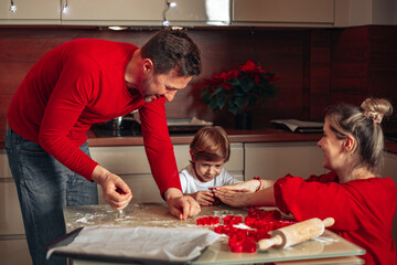 Dad, mom and child, boy 4 years old. Have fun in kitchen, bake Christmas cookies, dressed in red clothes. Cozy atmosphere of happiness. Teamwork