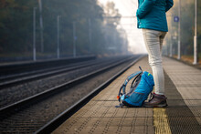 Solo traveler waiting for train at empty railroad station. Woman with backpack standing at railway platform