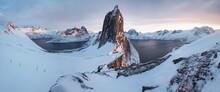 Scenic View from Mount Hesten on Iconic Mountain Segla at dawn in winter with snow in front of colorful sky and mountain range in background, Fjordgard, Mefjorden, Senja, Norway