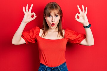 Sticker - Redhead young woman wearing casual red t shirt looking surprised and shocked doing ok approval symbol with fingers. crazy expression