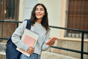 Wall Mural - Young middle east student girl smiling happy using smartphone at the city.