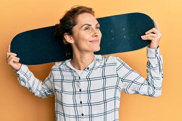 Canvas Print - Young brunette woman holding skate smiling looking to the side and staring away thinking.