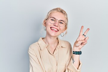 Canvas Print - Beautiful caucasian woman with blond hair wearing casual look and glasses smiling with happy face winking at the camera doing victory sign. number two.