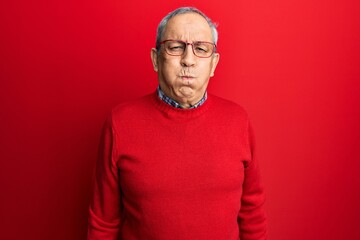 Wall Mural - Handsome senior man with grey hair wearing casual clothes and glasses puffing cheeks with funny face. mouth inflated with air, crazy expression.