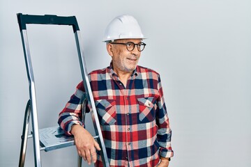 Poster - Handsome mature handyman close to construction stairs wearing hardhat smiling looking to the side and staring away thinking.