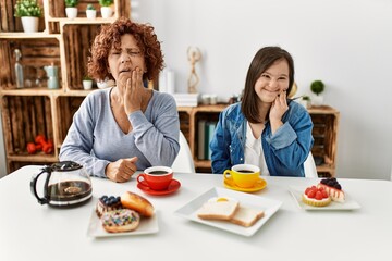 Canvas Print - Family of mother and down syndrome daughter sitting at home eating breakfast touching mouth with hand with painful expression because of toothache or dental illness on teeth. dentist