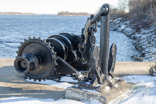 Heavy Black Iron Ship's Anchor, Chain And Windlass On A Concrete Pier With Snow, Daytime, Nobody