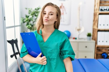 Sticker - Young caucasian woman working at pain recovery clinic looking at the camera blowing a kiss on air being lovely and sexy. love expression.