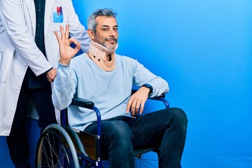 Canvas Print - Handsome middle age man with grey hair on wheelchair wearing cervical collar smiling positive doing ok sign with hand and fingers. successful expression.