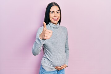 Poster - Beautiful woman with blue eyes expecting a baby, touching pregnant belly approving doing positive gesture with hand, thumbs up smiling and happy for success. winner gesture.